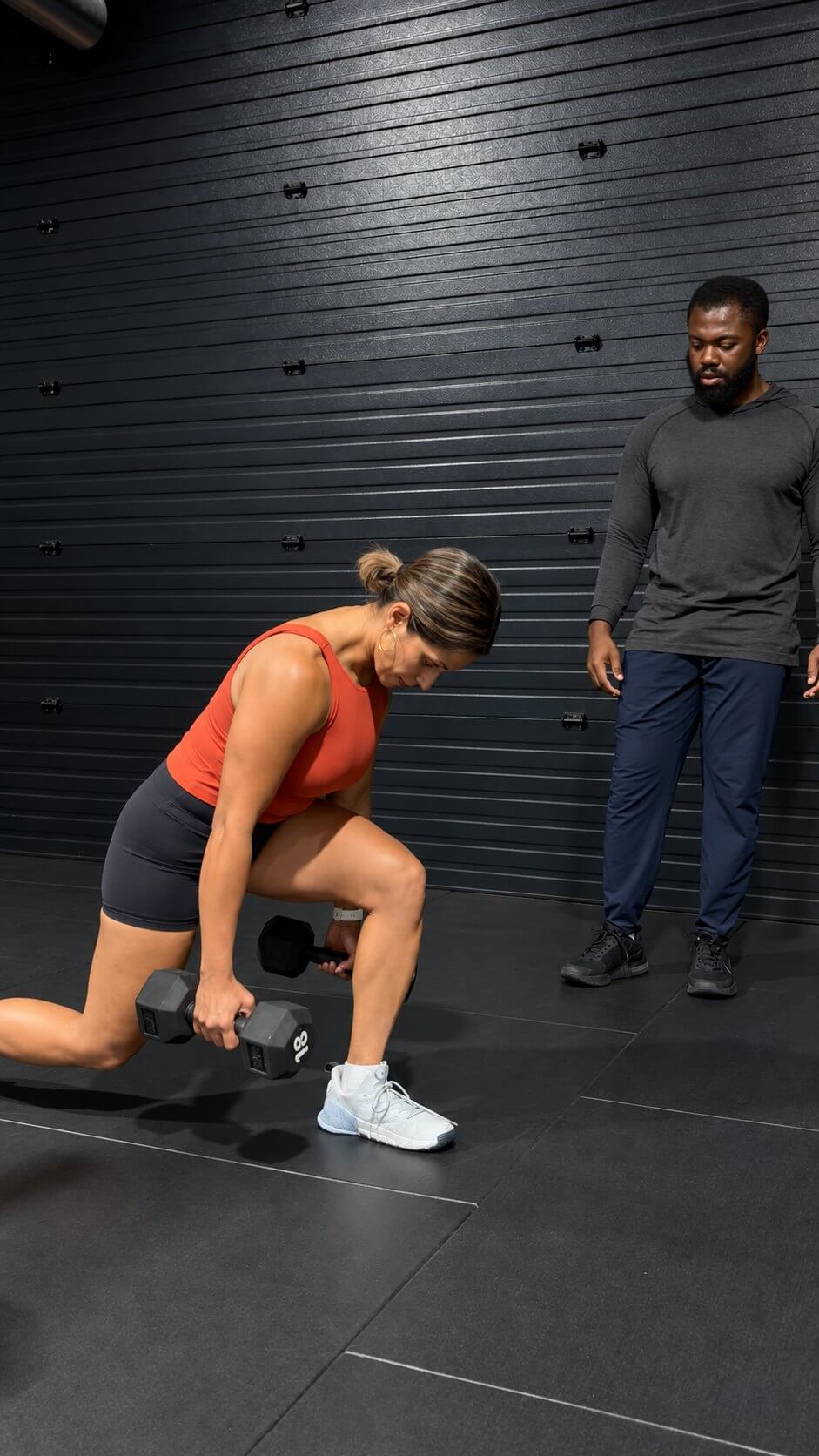 Doug watching a client's form as she lunges with dumbbells.